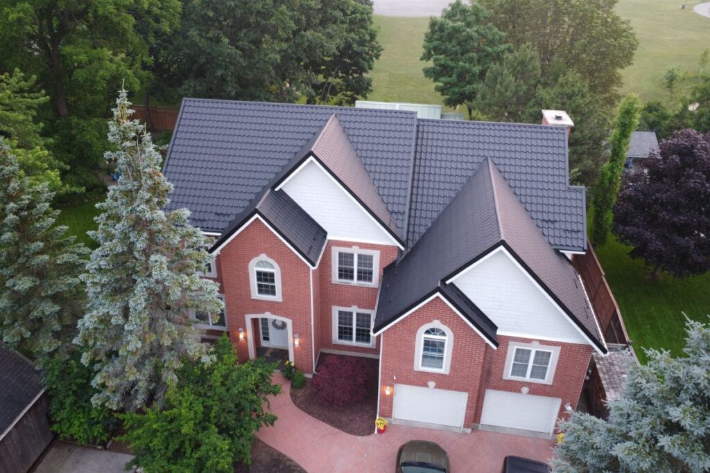 Brick home with a black metal roof and lush green trees surrounding the yard.