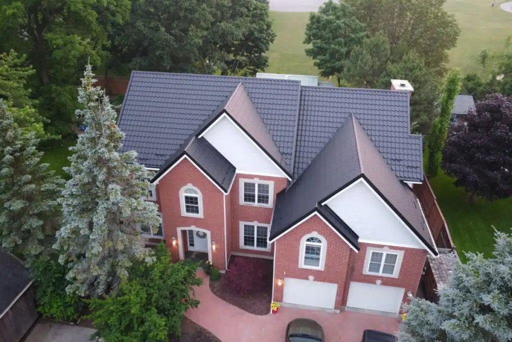 Brick home with a black metal roof and lush green trees surrounding the yard.