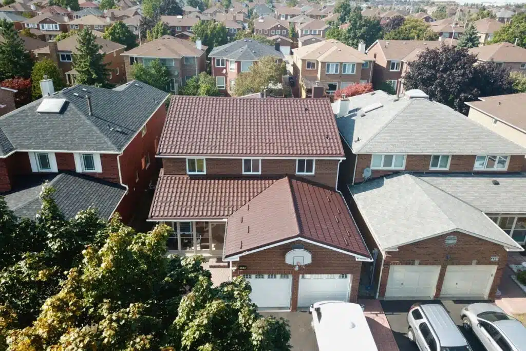 Aerial shot of a brown metal roof on a home with a unique design, contrasting with neighboring homes and a clear blue sky.