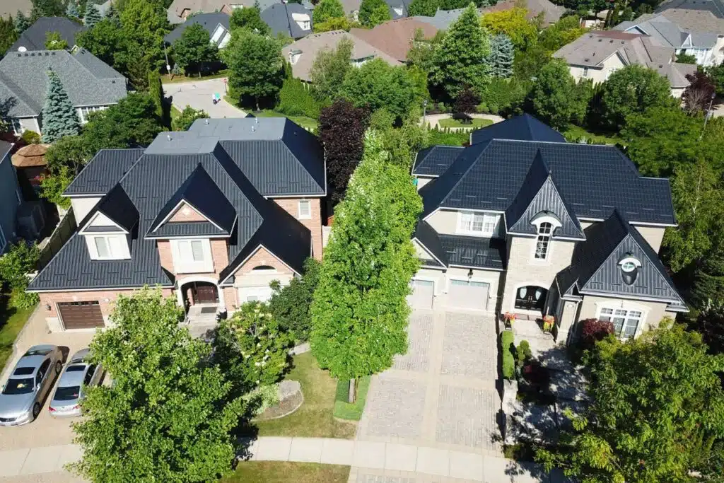 An aerial view of two homes with sleek black metal tile roofs, showcasing beautifully landscaped yards and neatly paved driveways.