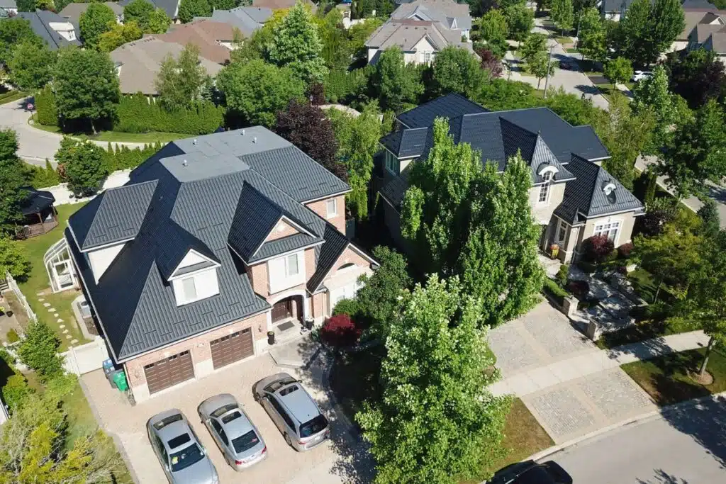 Stunning aerial view of two homes with newly installed black metal tile roofs, highlighting the beautiful landscaping and well-maintained driveways.