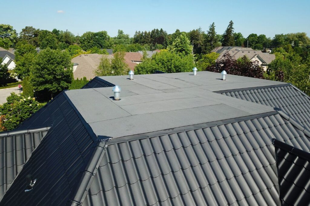 Flat section of a newly installed metal roof, featuring sleek black tiles with ventilation pipes, seamlessly blending into the rest of the roofing system.
