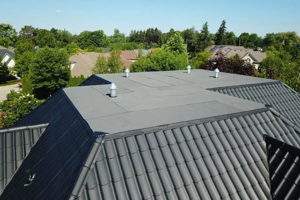 Flat section of a newly installed metal roof, featuring sleek black tiles with ventilation pipes, seamlessly blending into the rest of the roofing system.