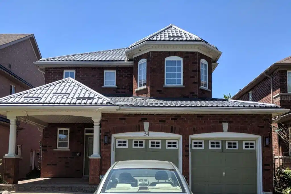 A charming home with a sleek dark gray metal roof, highlighting its elegant, angular design over a well-maintained brick exterior.