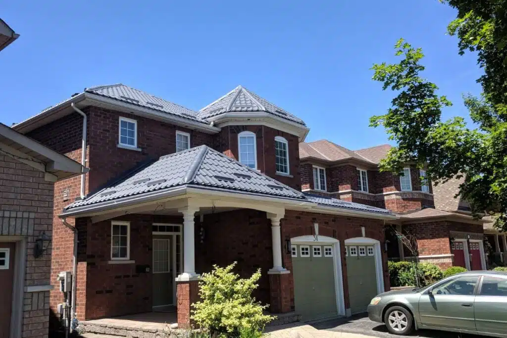 New metal roof installation on a house with a unique design, featuring dark gray roofing panels and white columns.