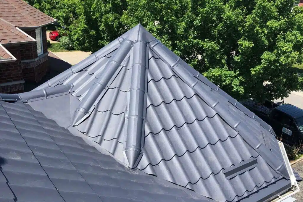 High-angle shot of a dark gray textured metal roof showing ridges, valleys, and ventilation features.