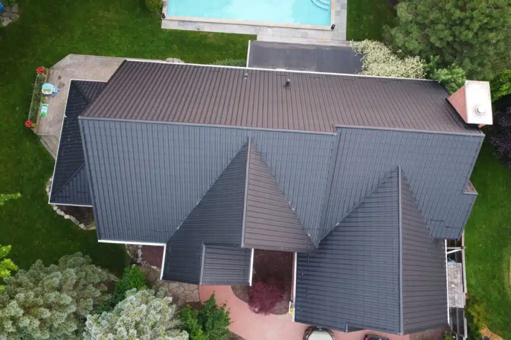 Top-down view of a home with a dark metal roof, featuring a triangular roof peak, green yard, and a pool.