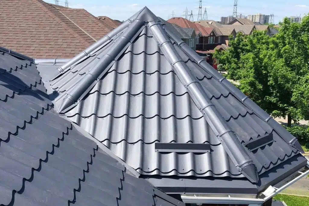 Close-up of a gray metal roof with well-defined ridges, showing ventilation features and neighboring roofs.