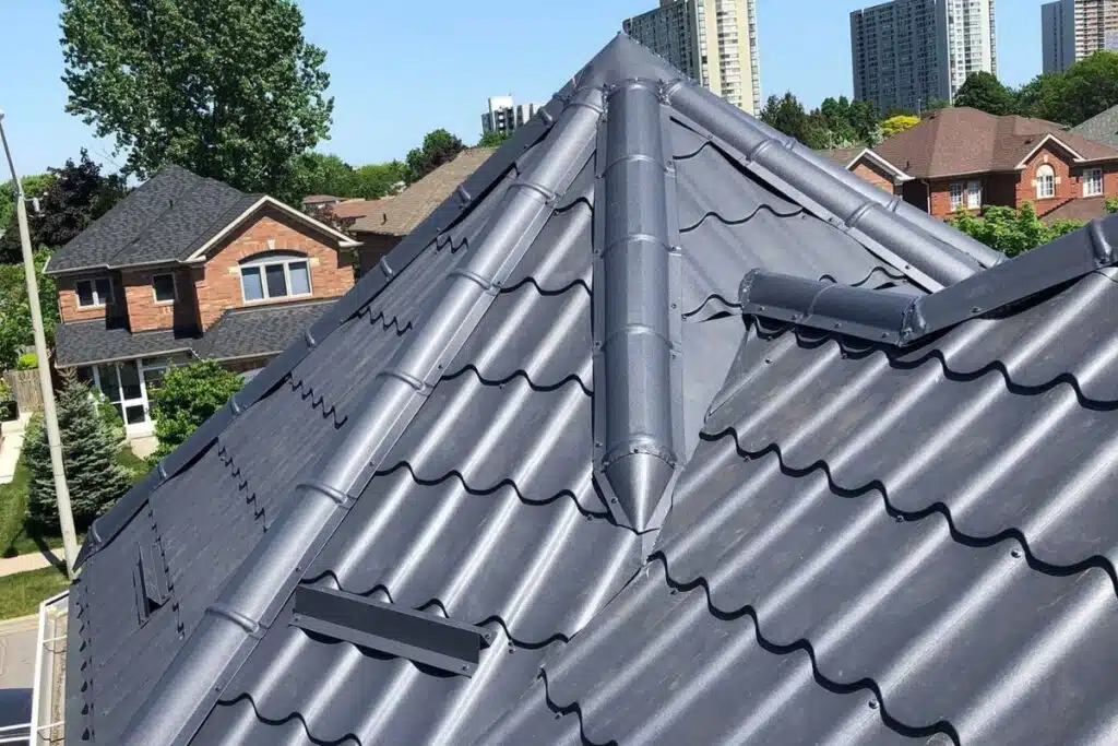 Close-up of a modern Monterrey metal roof with a grey finish, highlighting the tiles and vents, with a backdrop of suburban houses.