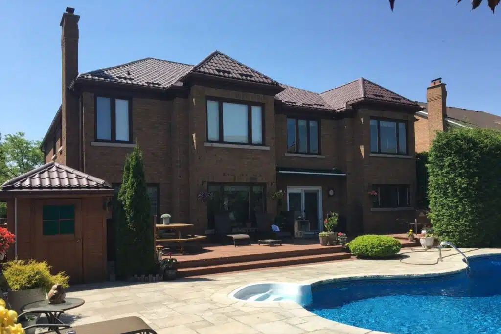 Home with a brown metal roof, showcasing a backyard with a pool and a wooden deck surrounded by greenery.