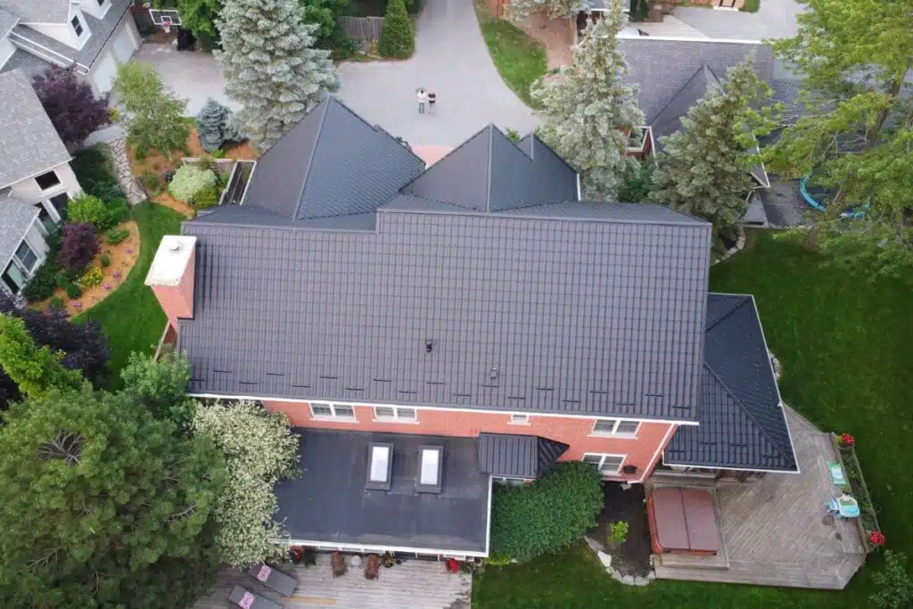 Aerial view of a home with a sleek dark metal roof, lush green yard, and a cozy backyard patio area with a hot tub.