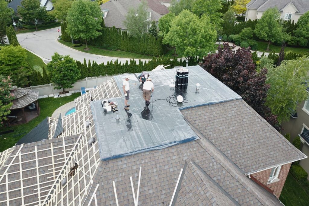 Roofing project in progress, with workers applying a protective layer to the roof structure, preparing for metal tile installation.