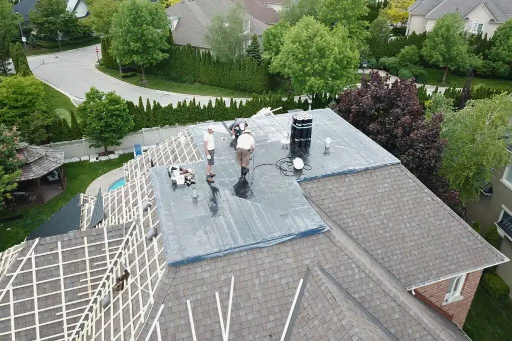 Roofing project in progress, with workers applying a protective layer to the roof structure, preparing for metal tile installation.