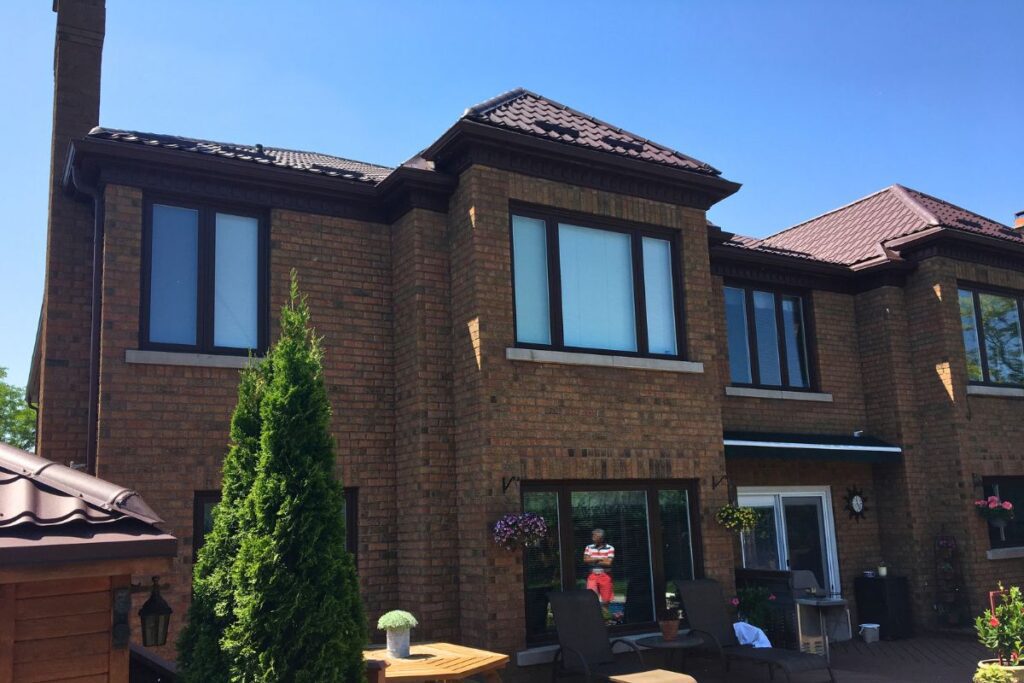 Side view of a home with a brown metal roof, showcasing large windows and a well-maintained backyard garden.