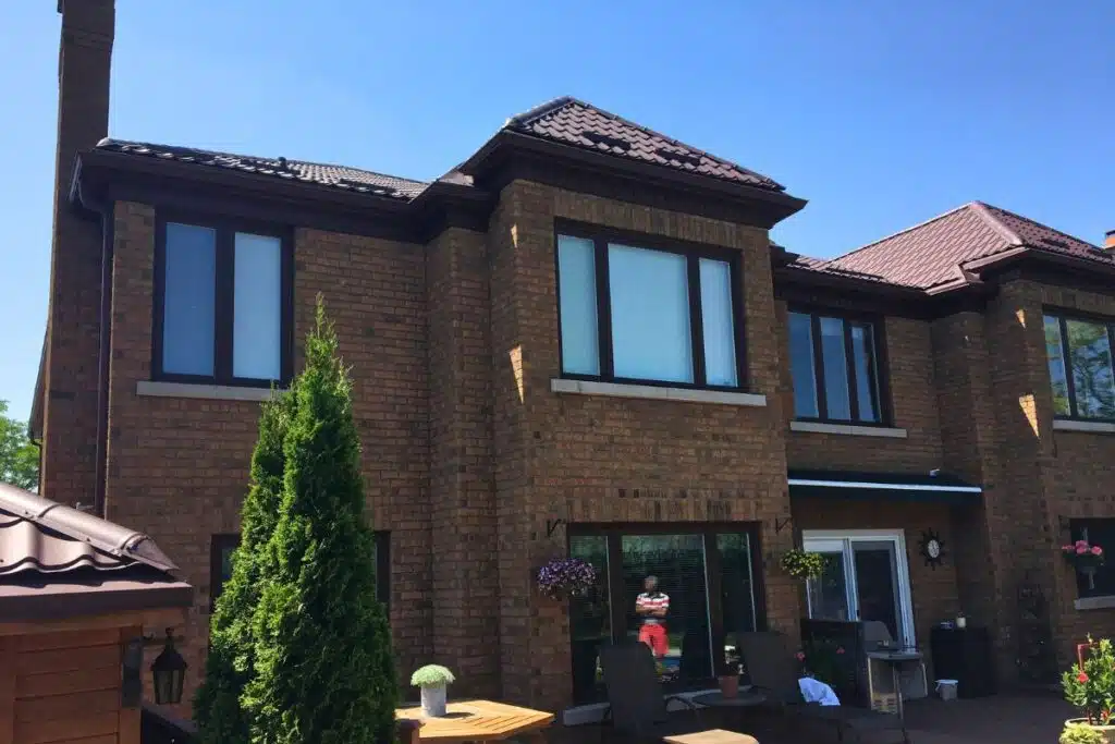 Side view of a home with a brown metal roof, showcasing large windows and a well-maintained backyard garden.