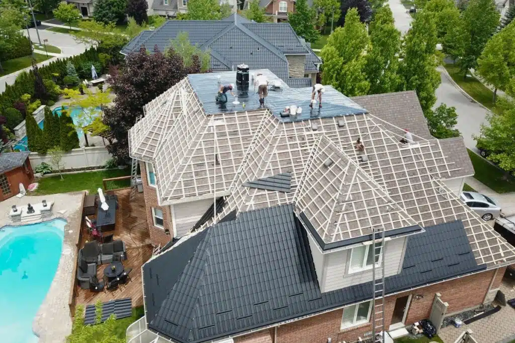 Aerial view of a roof replacement project in progress, with workers on a wooden-framed roof, preparing it for the installation of metal tiles.