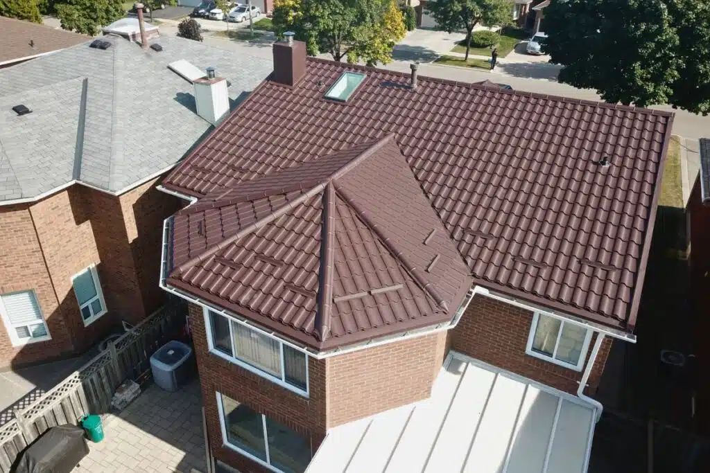 View of a completed brown metal roof with skylight and vent, showing a smooth transition between sections.