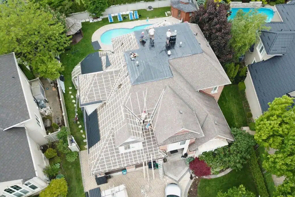 Aerial view of a home in the middle of a roof replacement, with workers removing the old shingles and preparing the structure for new metal tiles.