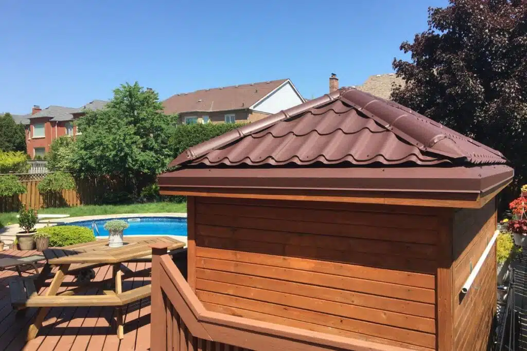 A wooden shed with a newly installed brown metal roof, situated near a pool and patio area in a residential backyard.