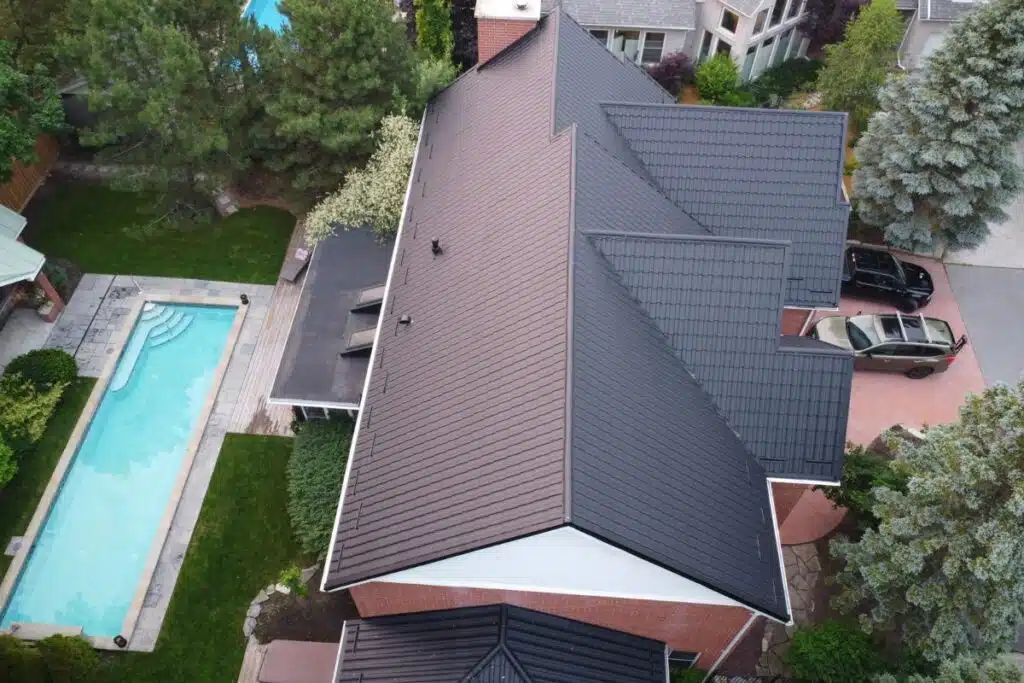 A bird’s-eye view of a modern home with a dark metal roof, overlooking a backyard pool and lush green trees.