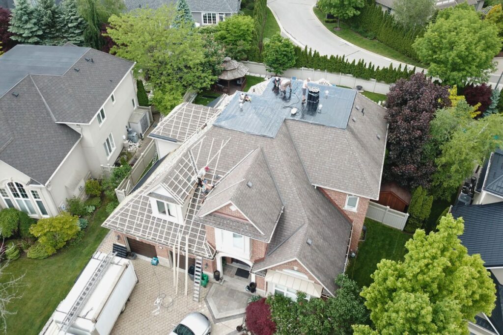 An aerial view of a home under roof replacement, showcasing the removal of old shingles and preparation of the roof for metal tiles.