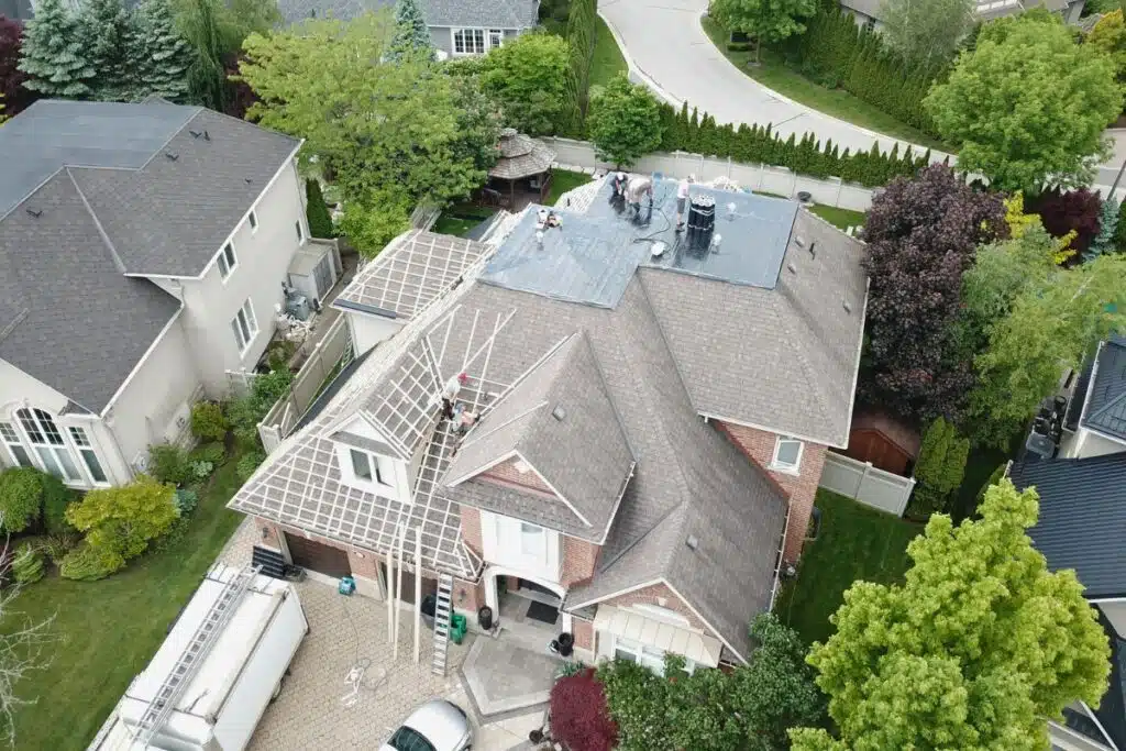 An aerial view of a home under roof replacement, showcasing the removal of old shingles and preparation of the roof for metal tiles.