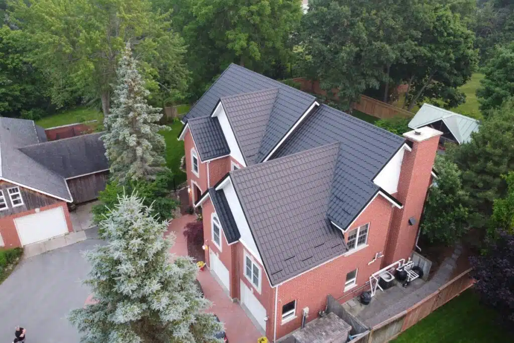 A top-down view of a large home featuring a sleek black metal roof, surrounded by greenery and trees.