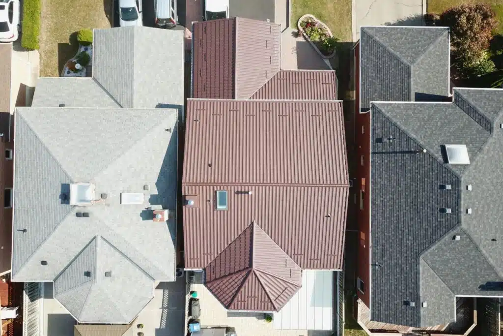 Aerial view showing a newly installed brown metal roof alongside neighboring homes with traditional shingle roofs.