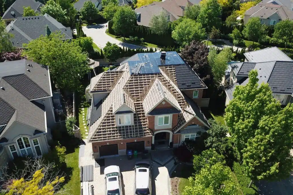 A bird's-eye view of a home with an ongoing roof replacement, showing the wooden trusses and an area of the roof covered with metal tiles.