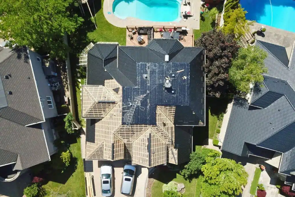 An aerial view of a home under construction, showcasing a partially completed roof with wooden trusses, and a beautiful pool area in the background.