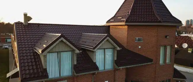 Close-up view of a red-tiled roof with a distinctive turret and large windows.