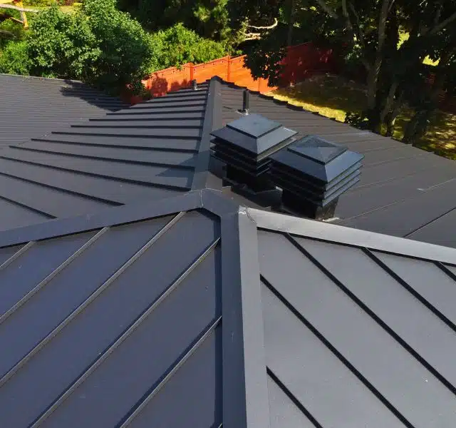 Close-up view of a black metal roof with distinct ridges and two roof vents.