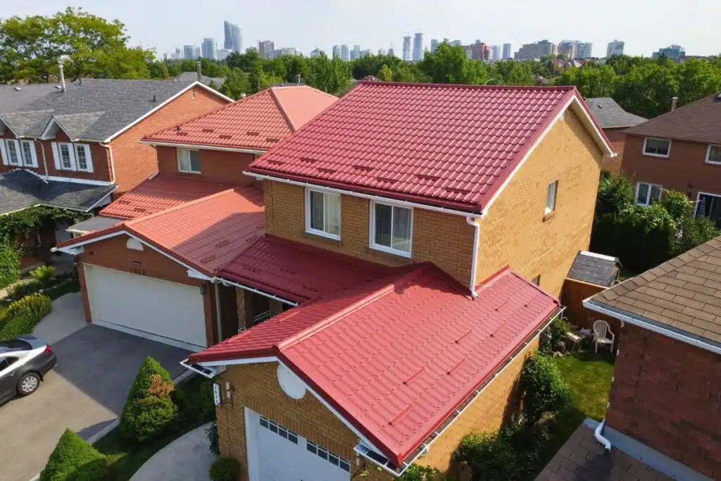 Two-story yellow brick house with a red Monterrey metal roof, white-framed windows, and a double garage, set in a suburban neighborhood with a city skyline in the background.