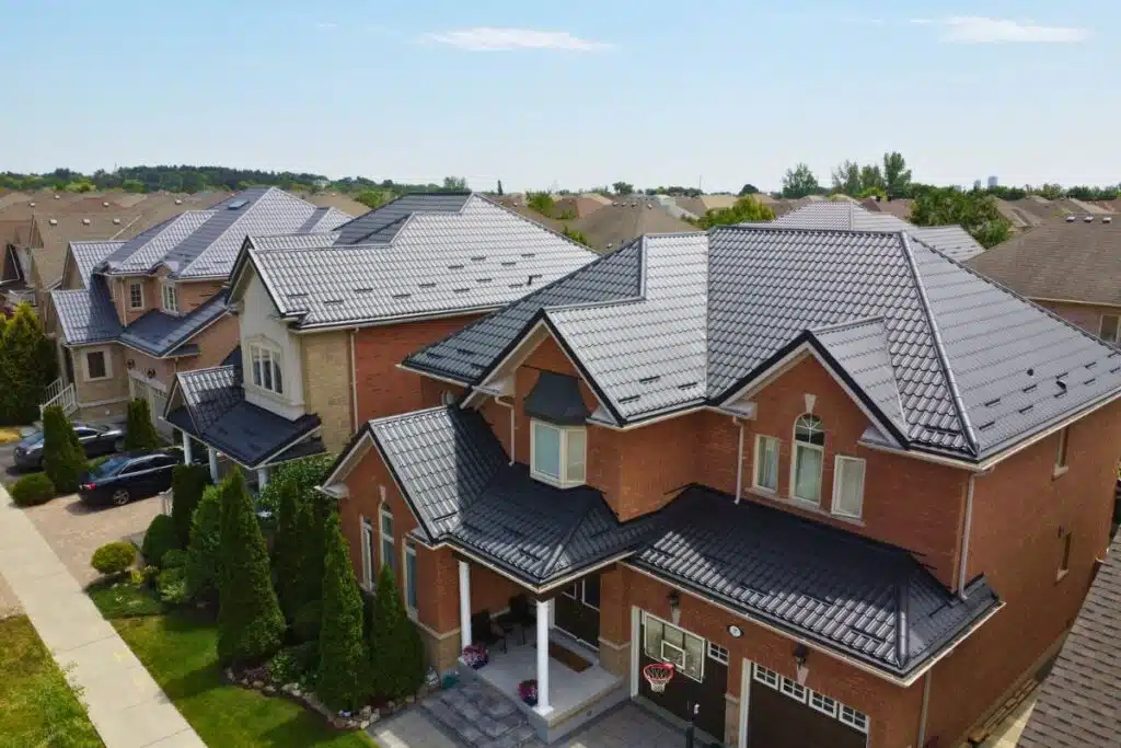 Row of red and beige brick houses with dark grey Monterrey metal roofs, featuring large windows and well-maintained front yards in a suburban neighborhood.