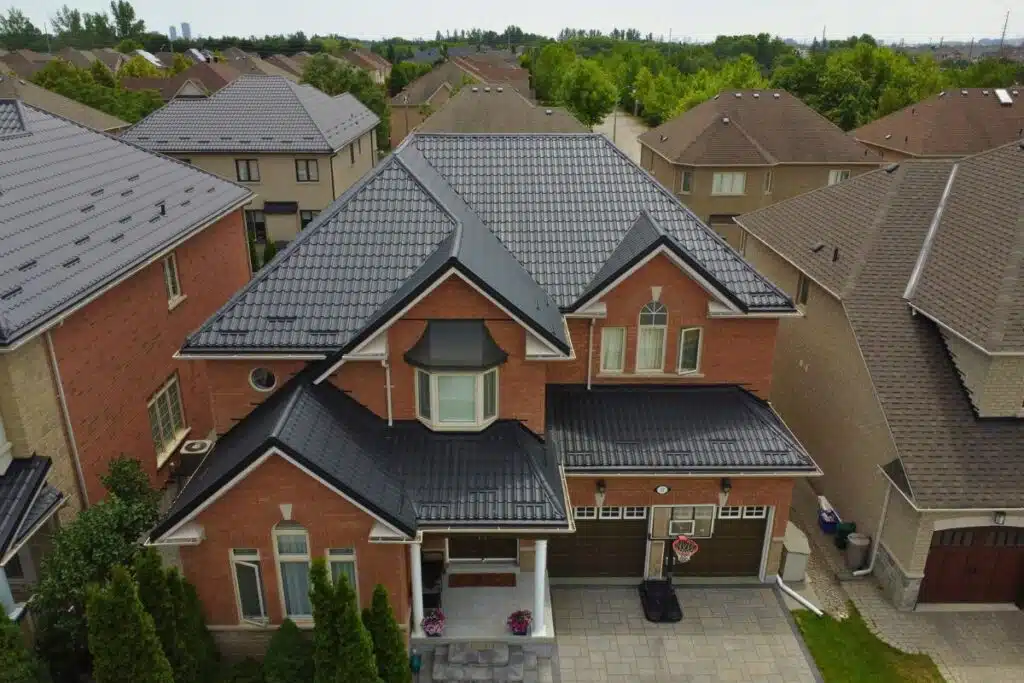 Two-story red brick house with a dark grey Monterrey metal roof, arched windows, and a covered front entrance, situated in a residential neighborhood.
