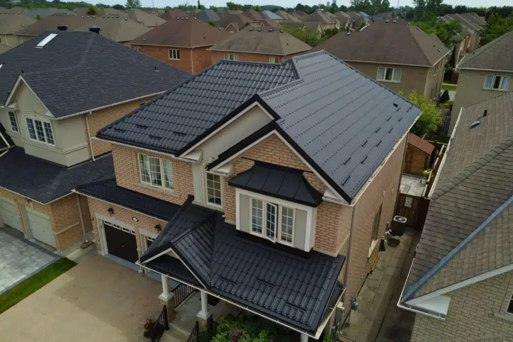 Beige two-story house with a dark grey Monterrey metal roof, black accents, and large windows, situated in a suburban neighborhood.