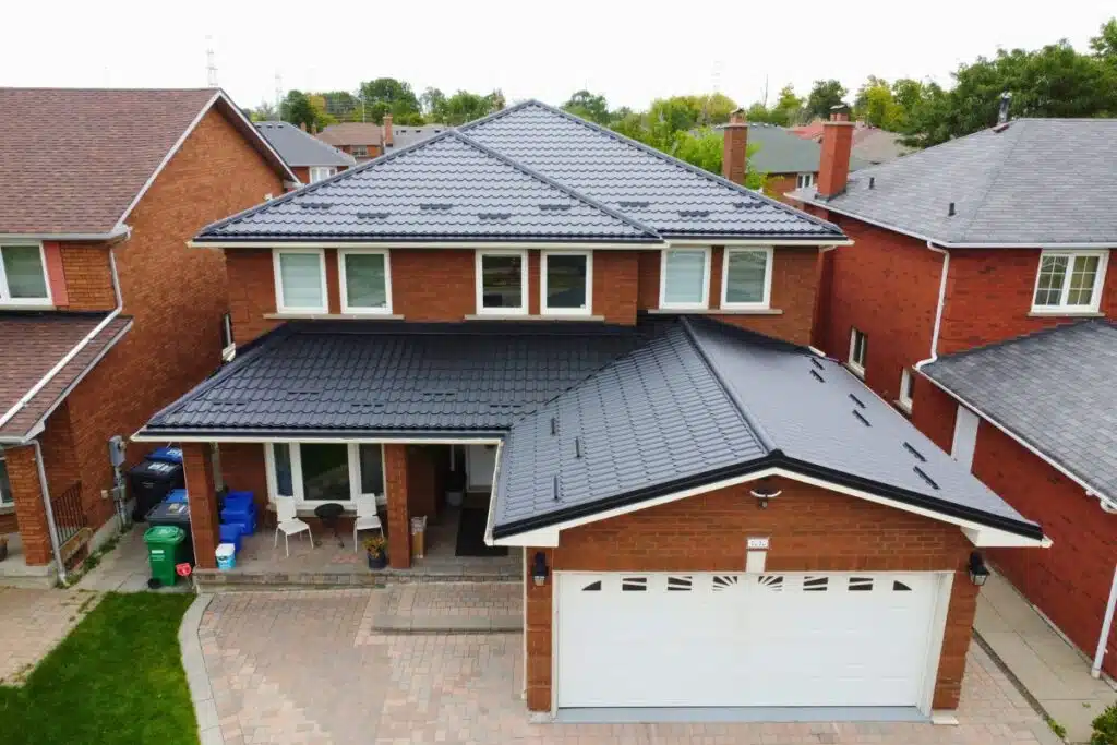 Two-story red brick house with a dark grey Monterrey metal roof, a covered front porch, and a white double garage door.