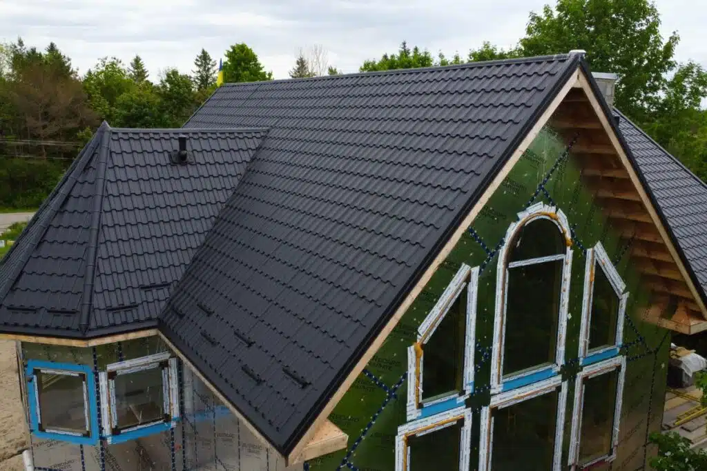 New Adamante Metal Roof for Modern Homes House under construction with large arched windows and a newly installed dark grey Adamante metal roof, surrounded by greenery.