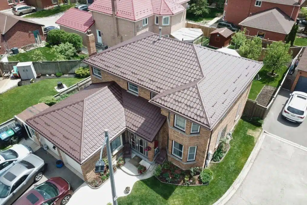 Elegant Adamante Metal Roof for Homes in Toronto Large two-story brick house with a brown Adamante metal roof, surrounded by a green lawn, flower beds, and neighboring homes.