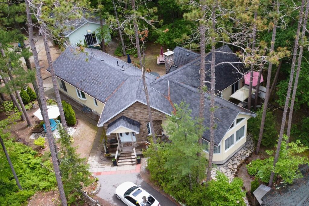 Top-down view of a home with a dark gray shingle roof, surrounded by trees and a stone pathway.