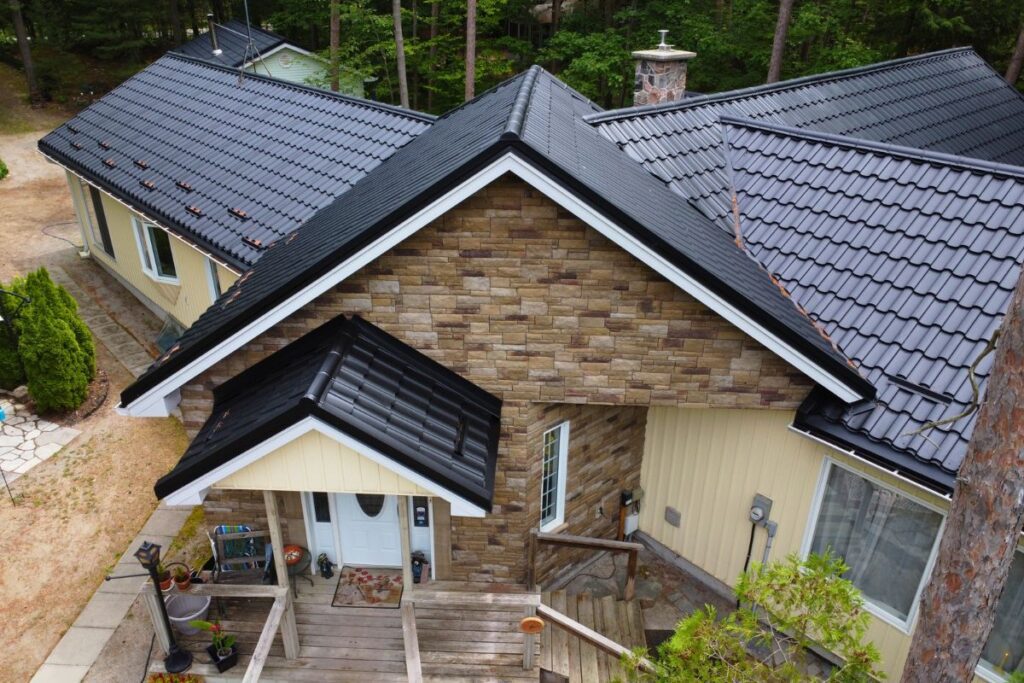 Front view of a house in Tiny Township featuring stone façade and black metal roof panels with a complex gable design and a welcoming front porch.