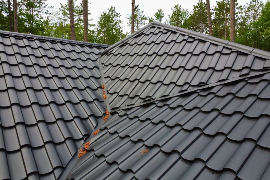 Close-up view of intersecting black metal roof slopes with small debris along the seam, highlighting the smooth texture and neat appearance of the roof tiles.