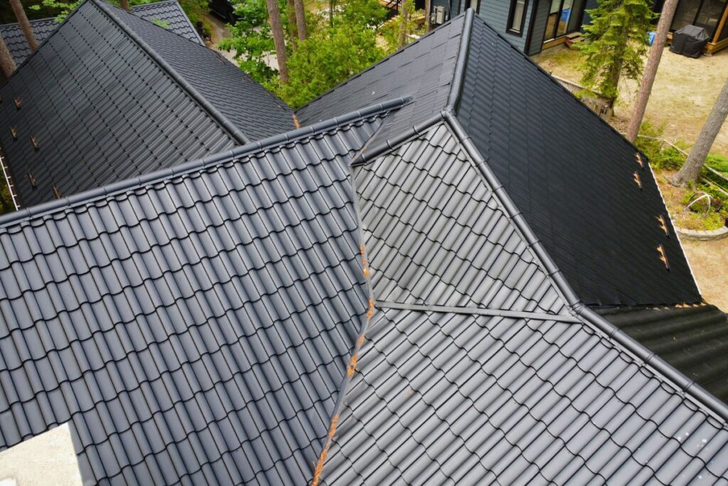 Aerial view of a black metal roof with multiple intersecting slopes, demonstrating the craftsmanship of a roof with sleek and durable tiles.