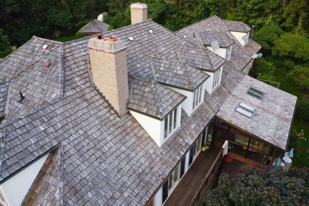 Aged cedar roof with shingles and chimneys on a multi-gabled house.