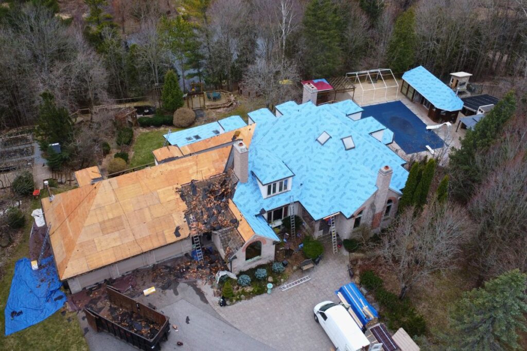 Aerial view of a roof replacement project with old cedar shingles being removed and waterproofing applied.