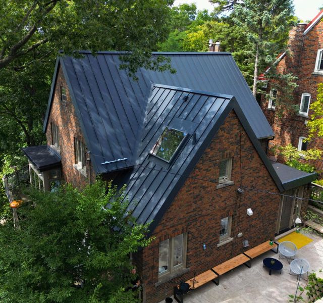 Finished standing seam metal roof on a brick home, showing skylight integration, clean panel layout, and flashing details.