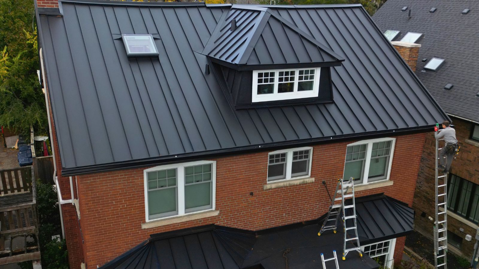 Completed standing seam metal roof with a VELUX skylight, front dormer, and lower entrance roof section