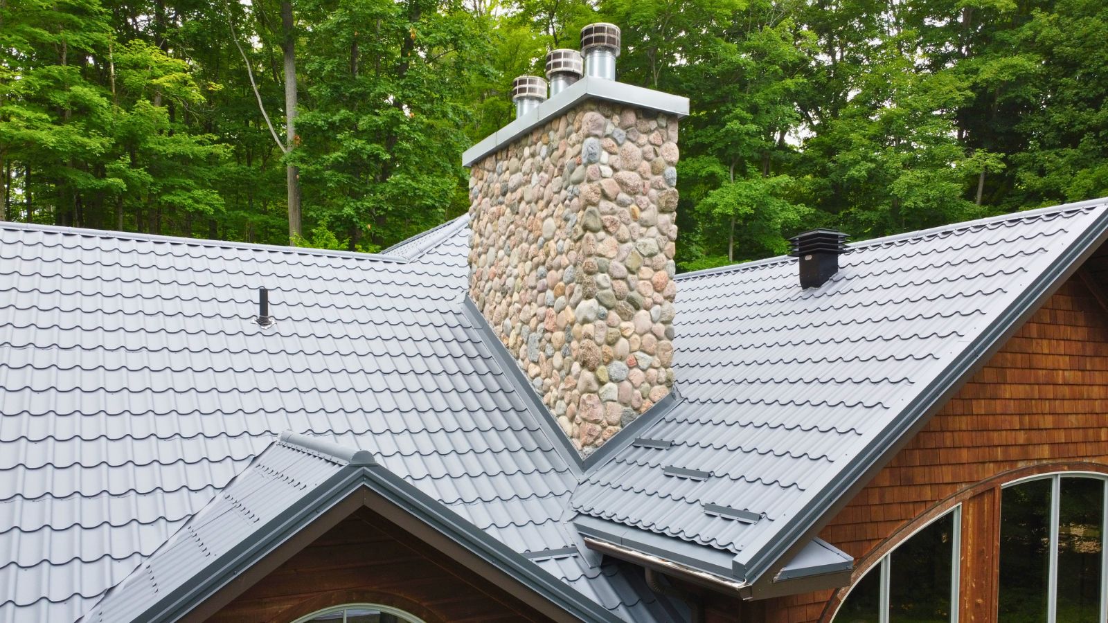 Stone chimney and roof transition detail on a RR22 Grey metal tile roof in Tiny Township